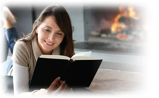 İçten ve rahat bir ortamda kitap okuyan mutlu bir kadın, arka planda şömine ve yumuşak bir aydınlatma var